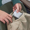 Person opening a beige bag with a small white device inside, sitting on a textured green surface.