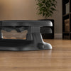 A close-up of an ergonomic foot rest on a wooden floor in a home setting, with a plant and shelving visible in the background.